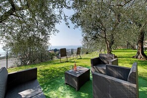 An outdoor seating area with wicker furniture, a bottle, and a glass, surrounded by trees and a view of the sea. - Giardini Di Corte - Standard Bed and Breakfast with Lake View, Wi-Fi, and Air Conditioning (Toscolano Maderno)