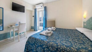Habitación de hotel con cama, escritorio, silla, televisor y ventana con cortinas.