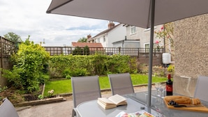 A glass table with a book, wine, and food under an umbrella in a garden setting. - Buckingham House Modern Coastal 3BR Stay (Morecambe)