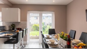 A modern kitchen with a dining area, a view through a glass door, and a table set for a meal. - Buckingham House Modern Coastal 3BR Stay (Morecambe)