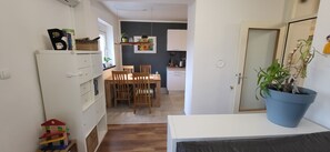 A compact kitchen with white cabinets, a wooden dining table, and chairs. There is a potted plant on the right. - 5 minutes' walk to the arena 🏛️ | Cozy family apartment + parking space & loggia (Pula)