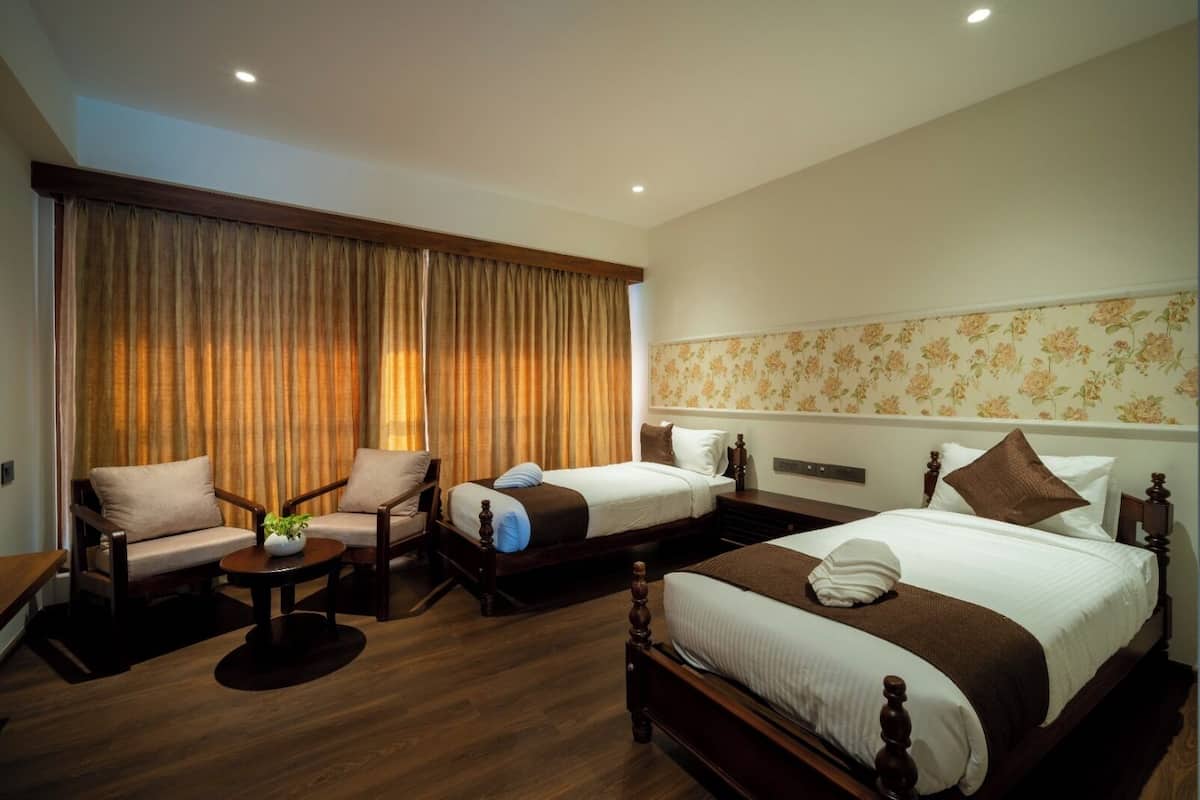 A hotel room with two single beds, a sofa, a small table with a plant, and a large window with curtains.