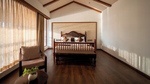 A bedroom with a wooden bed, a chair, a small table with a plant, and a large window with curtains. - VIHARA By CMK (Kanayannur)