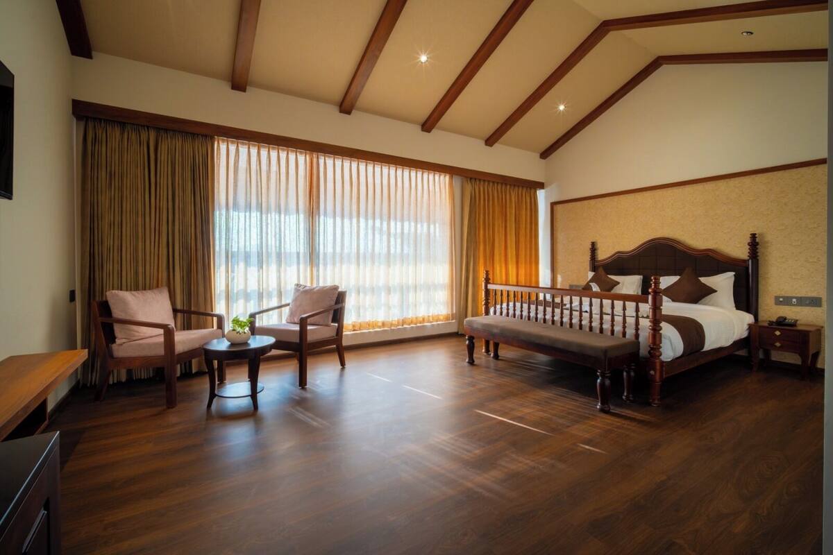 A hotel room with a wooden bed, two armchairs, a bench, a small table with a plant, and a nightstand.