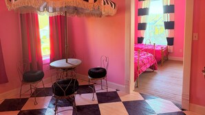 A room with a checkered floor, a round table with chairs, a striped umbrella, and a bed with a pink bedspread. - Beautiful Creekside loft over Historic Mannington  (Mannington)