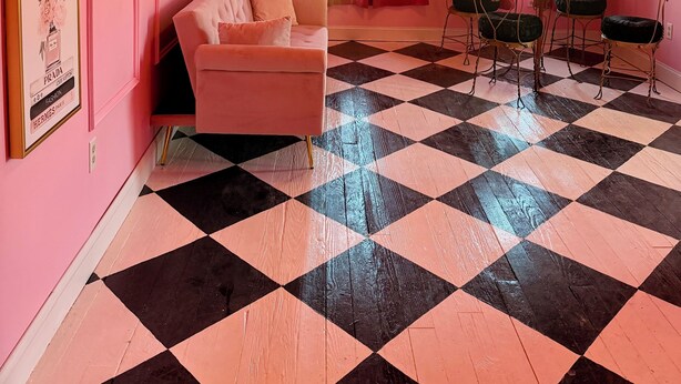 A room with a pink wall, a checkered floor, a ceiling fan, a chandelier, a sofa, a table with chairs, and a window with curtains. - Beautiful Creekside loft over Historic Mannington  (Mannington)