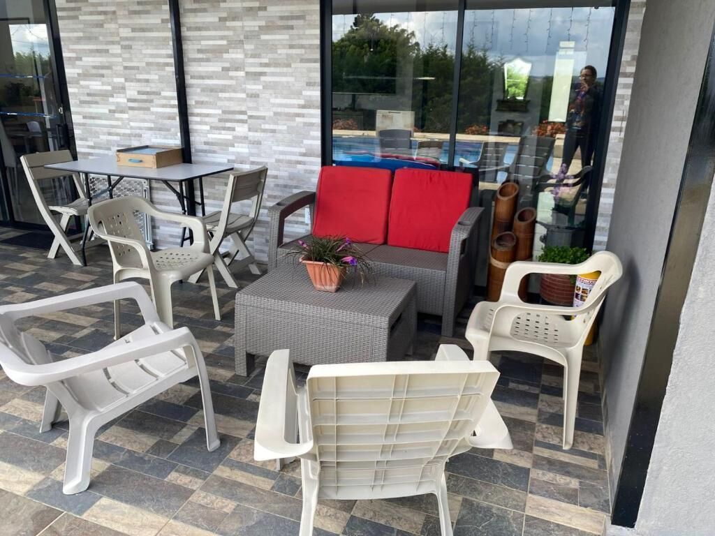 Une terrasse extérieure aménagée avec des meubles en osier, un canapé gris agrémenté de coussins rouges et une petite table sur laquelle est posée une plante.