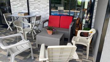 Un patio exterior con mobiliario de mimbre, un sofá gris con cojines rojos y una mesita con una planta.