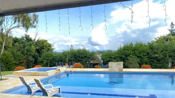 Une piscine entourée de chaises longues, de verdure et d’un espace abrité.