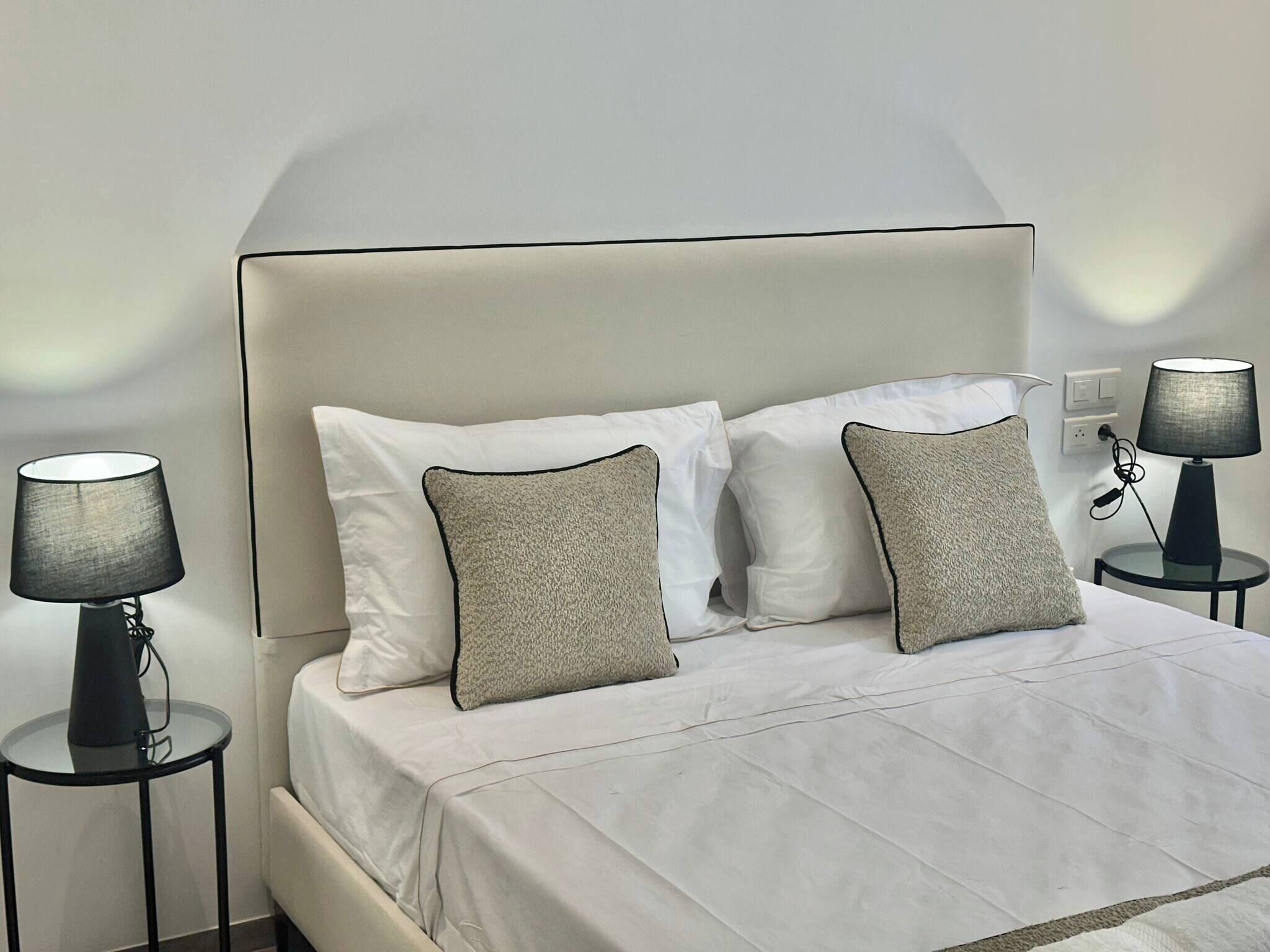 A bed with white bedding, two pillows, two bedside lamps, and a wall socket.