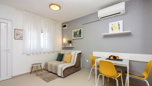 A modern living room with a sofa, a dining table with chairs, a small round table, and a wall-mounted air conditioner. - Attic apartment with WiFi, air conditioning and private parking space (Crikvenica)