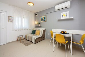 A modern living room with a sofa, a dining table with chairs, a small round table, and a wall-mounted air conditioner. - Attic apartment with WiFi, air conditioning and private parking space (Crikvenica)