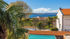 A coastal view with a swimming pool, palm trees, and a building with a tiled roof. - Attic apartment with WiFi, air conditioning and private parking space (Crikvenica)