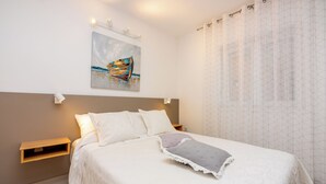 A neatly made bed with a pillow, a bedside table, a wall-mounted light, and a painting above the bed. - Attic apartment with WiFi, air conditioning and private parking space (Crikvenica)