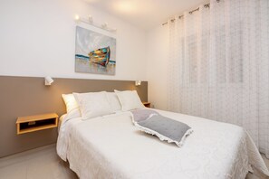 A neatly made bed with a pillow, a bedside table, a wall-mounted light, and a painting above the bed. - Attic apartment with WiFi, air conditioning and private parking space (Crikvenica)