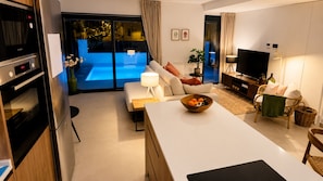 Een moderne woonkamer met een bank, een eettafel, een televisie en een keukenhoek met een koelkast en oven.