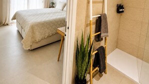 A modern bedroom with a large bed, a small table, a ladder, a potted plant, and a bathroom with a shower and toilet. - Casa Salina del Sol – Private Pool & Terrace (San Pedro del Pinatar)