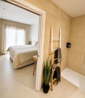 Een moderne slaapkamer met een groot bed, een klein tafeltje, een ladder, een kamerplant en een badkamer met douche en toilet.