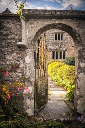 An arched stone gateway leading to a building with a garden pathway. - Wild Hamatethy (Bodmin)