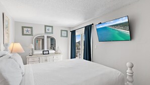 Een slaapkamer met een bed, een dressoir, een spiegel, een televisie en een raam met gordijnen.