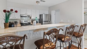 Een moderne keuken met witte kasten, roestvrijstalen apparatuur, een marmeren aanrechtblad en een bar met houten stoelen.
