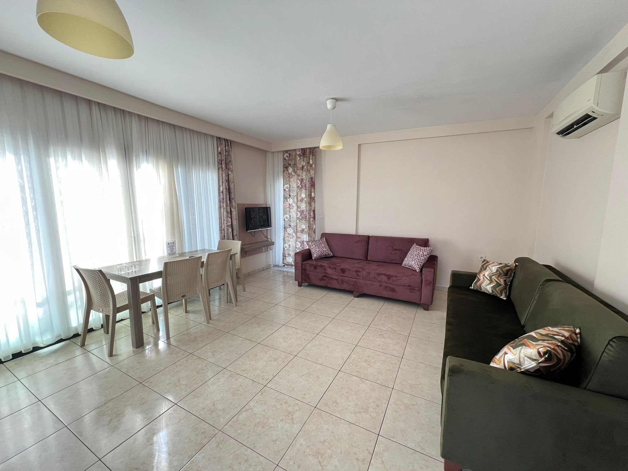 A living room with a dining table, two sofas, a TV, and a ceiling light.