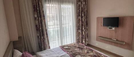 Un dormitorio con cama, cortinas, televisor y una lámpara en el techo.