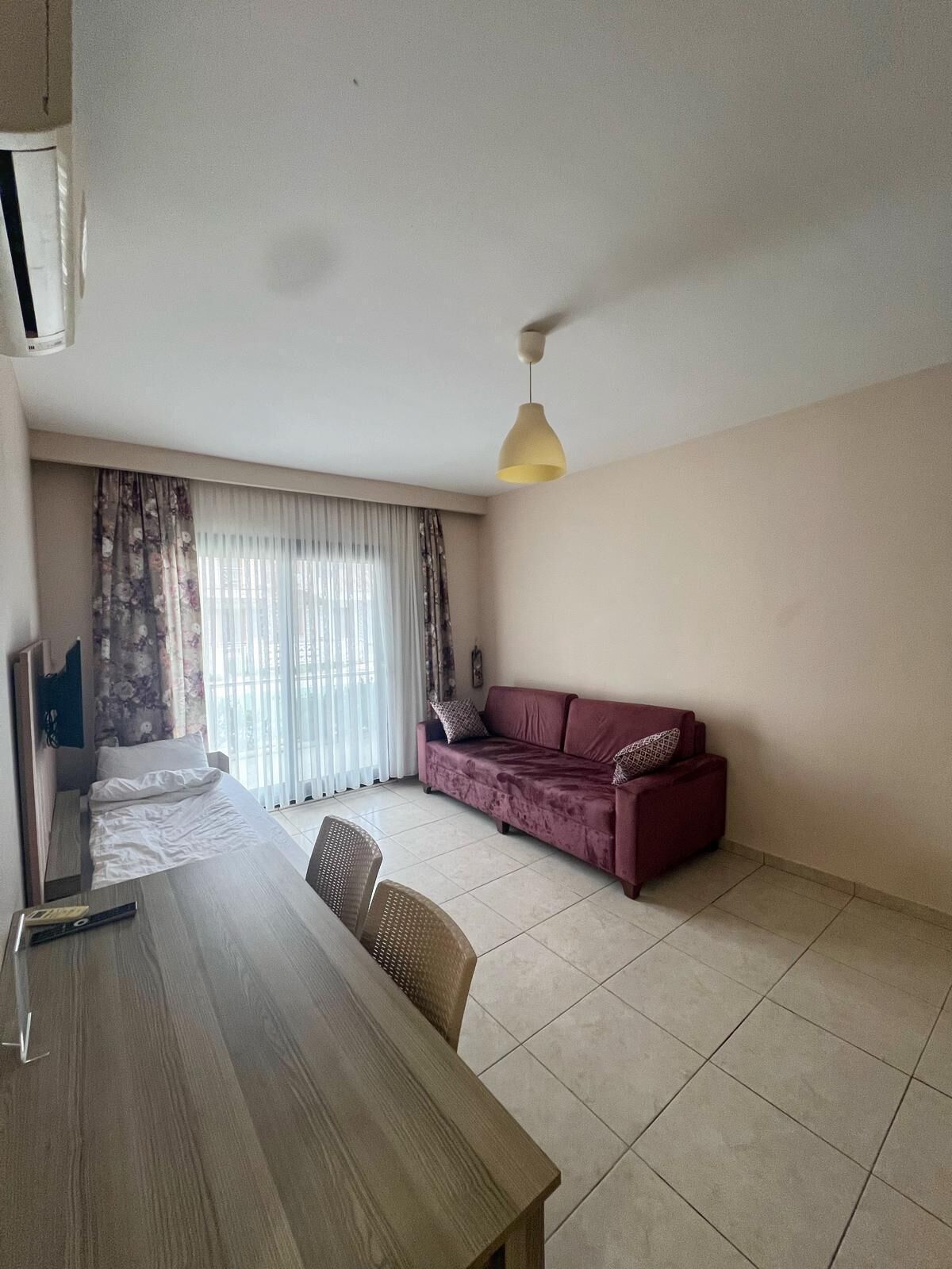 Ein Zimmer mit einem Bett, einem Sofa, einem Esstisch und einer Pendelleuchte.