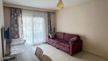 Ein Zimmer mit einem Bett, einem Sofa, einem Esstisch und einer Pendelleuchte.