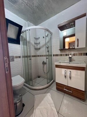 Un baño con ducha envuelta en vidrio, inodoro blanco, tocador con lavamanos y espejo sobre el tocador.