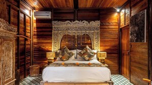 A wooden-paneled room with a bed, a carved wooden headboard, and a patterned floor. - Airlangga Dsawah by Balihora, Ubud Vill (Ubud)