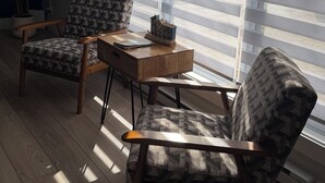 A room with two patterned armchairs, a small wooden table, and a large window with blinds. - Brigus Bay House (Brigus)