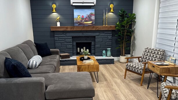 A modern living room with a fireplace, a sofa, a coffee table, and a patterned armchair. - Brigus Bay House (Brigus)