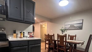 A modern kitchen with dark cabinets, a wooden dining table, and a view of the dining area. - Brigus Bay House (Brigus)