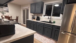 A modern kitchen with dark cabinets, a stainless steel refrigerator, and a marble countertop. - Brigus Bay House (Brigus)