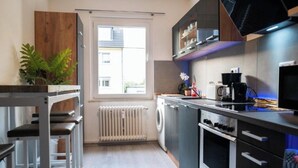 A modern kitchen with a built-in oven, a washing machine, and a window with a view of buildings. - Apartment Fioranza Comfortable stylish apartment for 6 people (Mülheim an der Ruhr)