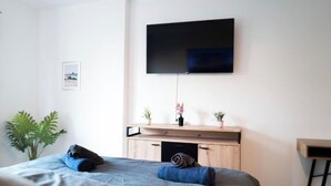 A bedroom with a bed, a TV mounted on the wall, a small wooden cabinet, and a potted plant. - Apartment Fioranza Comfortable stylish apartment for 6 people (Mülheim an der Ruhr)