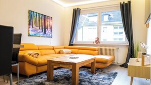 A modern living room with a sectional sofa, a wooden coffee table, a painting on the wall, and a window with curtains. - Apartment Fioranza Comfortable stylish apartment for 6 people (Mülheim an der Ruhr)