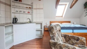 Een compacte kamer met een kitchenette, een bed met een blauwe matras en een gestreept fauteuil.