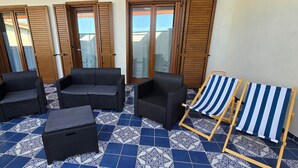 En uteplats med möbler i rotting, en randig strandstol och mönstrade golvplattor.