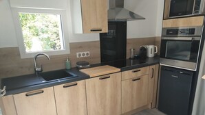 Uma cozinha moderna com armários de madeira, bancada preta, coifa de aço inoxidável, cafeteira e máquina de lavar louça.