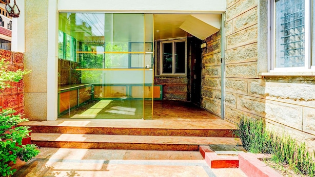 Una entrada moderna con puerta de cristal, paredes de piedra y un pequeño espacio exterior con escalones y plantas.