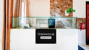 Un mostrador de recepción con un letrero que dice 'TOWNHOUSE Company Serviced', un panel de vidrio, una planta y un extintor.