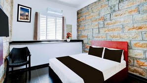 Un dormitorio con pared de ladrillo, cama con ropa de cama blanca y negra, ventana con persianas y una silla.