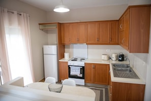 A compact kitchen with wooden cabinets, a white refrigerator, a stove, and a sink. - Loucas Home Kalloni Lesvos Central Stay w Balcony (Lesvos)