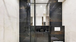 Et moderne badeværelse med en glasvæg omkring brusebadet, toilet og en håndvask med sort skål.