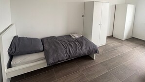 Et værelse med seng, garderobe og en lille bænk.