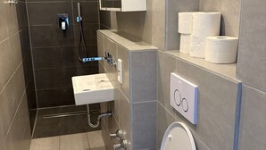Et moderne badeværelse med toilet, vask og bruseområde.