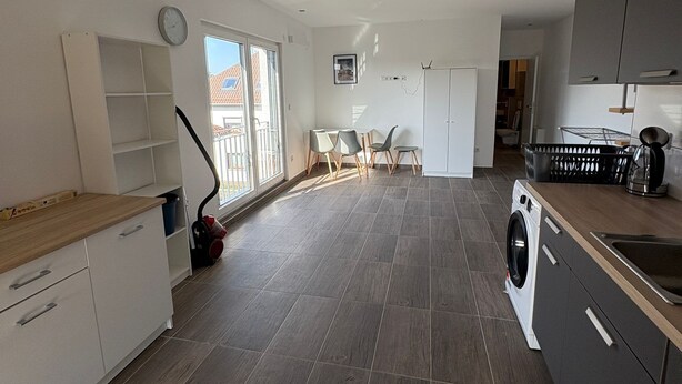 Et rummeligt køkken med vaskemaskine, vask og spiseplads med stole.