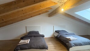 Et soveværelse med hems, to senge, træbjælker, et skydelys og et hvidt loft.